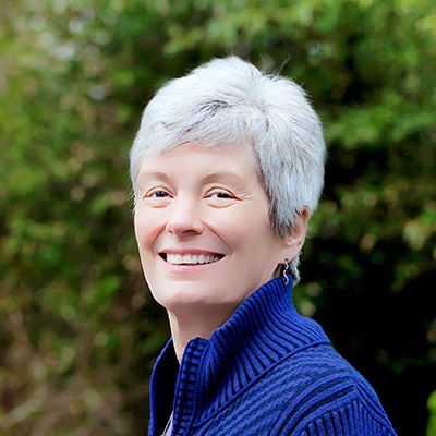 Headshot of Nancy L. She has short white hair and is wearing a blue half-zip sweater.